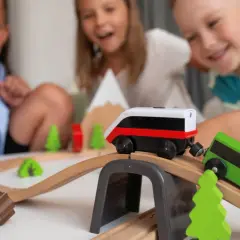 Dzieci bawią się drewnianymi pociągami na torach, tworząc własną kolejową przygodę.