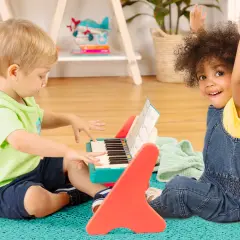 Dwóch chłopców bawi się przy kolorowym, drewnianym pianinie. Jeden gra, drugi z radością podnosi ręce.