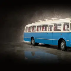 Niebiesko-biały autobus ogórek z bagażnikiem dachowym, stojący na mokrej nawierzchni.