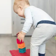Małe dziecko buduje wieżę z kolorowych klocków ceramicznych.