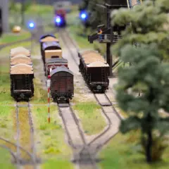 Miniaturowa kolej żelazna z wagonami towarowymi, zielenią i niebieskimi światłami sygnalizacyjnymi.