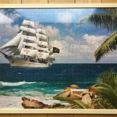 Ukończone puzzle na ścianie przedstawiają żaglowiec z czerwonymi krzyżami na białych żaglach, płynący po wzburzonym morzu.