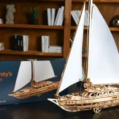 Drewniane modelarstwo: gotowy model żaglowca "Serenity's Dream" obok pudełka. Piękne detale i białe żagle.
