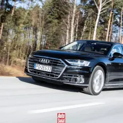 Czarne Audi A8 sunie po drodze wśród drzew. To jak układanie puzzli z luksusu i dynamiki.
