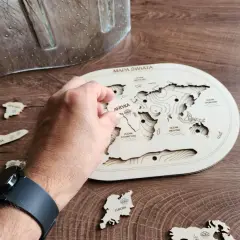 Dłoń układa drewniane puzzle kontynenty na mapie świata. Antarktyda i Europa czekają na swoje miejsce.