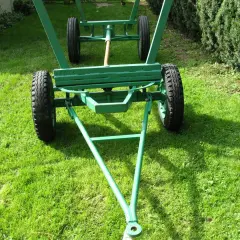 Zielony, dwukołowy wóz metalowy do ciągnika, gotowy do pracy na trawiastym podwórku.