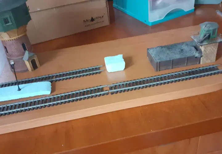 Diorama kolejowa z wieżą wodną, wagonem węglowym i budynkiem stacyjnym.