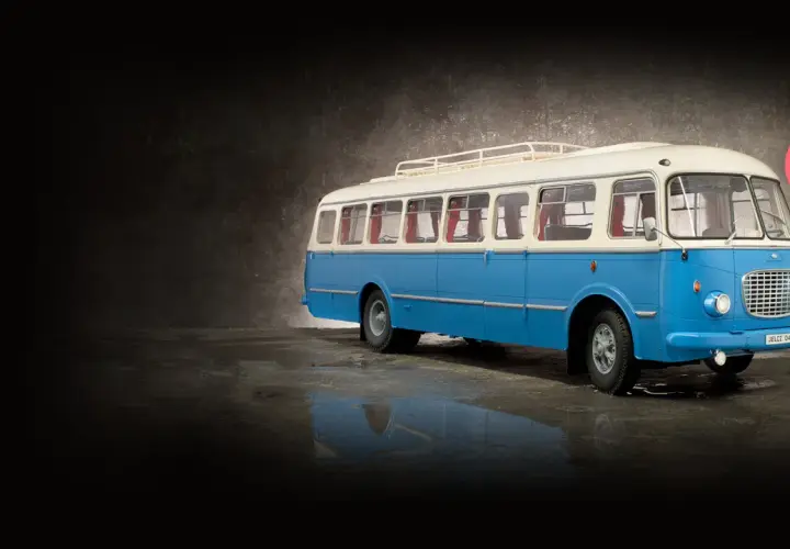Niebiesko-biały autobus ogórek z bagażnikiem dachowym, stojący na mokrej nawierzchni.