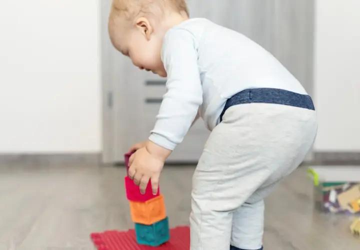 Małe dziecko buduje wieżę z kolorowych klocków ceramicznych.