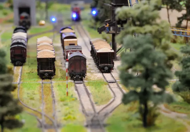 Miniaturowa kolej żelazna z wagonami towarowymi, zielenią i niebieskimi światłami sygnalizacyjnymi.