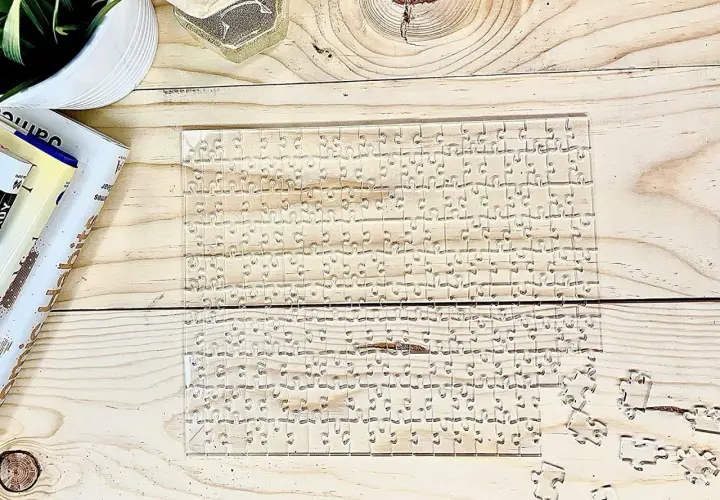 Przezroczyste, trudne puzzle na drewnianym blacie. Kilka elementów leży obok.