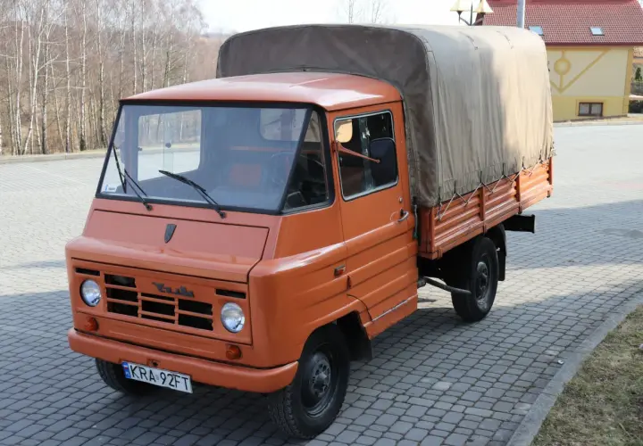 Pomarańczowy żuk z plandeką, gotowy do transportu towarów.
