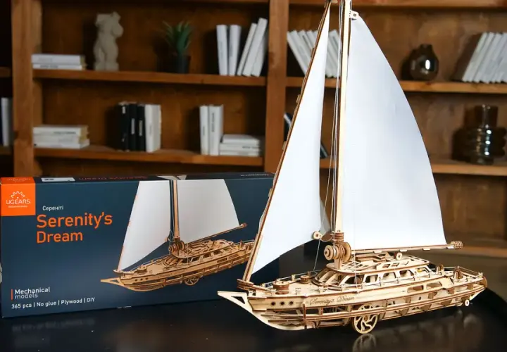 Drewniane modelarstwo: gotowy model żaglowca "Serenity's Dream" obok pudełka. Piękne detale i białe żagle.