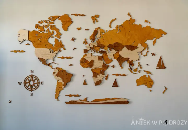 Drewniana mapa świata na ścianę, z zaznaczonymi krajami i oceanami. Kompas i żaglówki dodają jej podróżniczego charakteru.