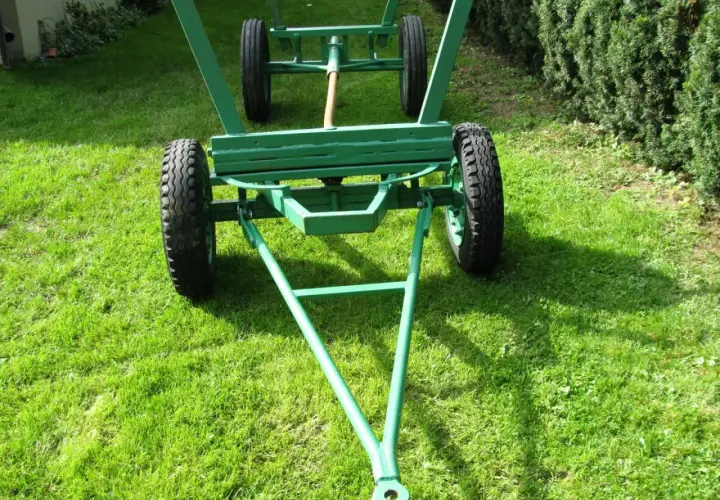 Zielony, dwukołowy wóz metalowy do ciągnika, gotowy do pracy na trawiastym podwórku.