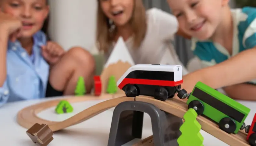 Dzieci bawią się drewnianymi pociągami na torach, tworząc własną kolejową przygodę.
