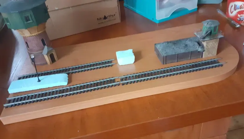 Diorama kolejowa z wieżą wodną, wagonem węglowym i budynkiem stacyjnym.