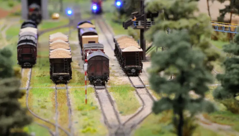Miniaturowa kolej żelazna z wagonami towarowymi, zielenią i niebieskimi światłami sygnalizacyjnymi.