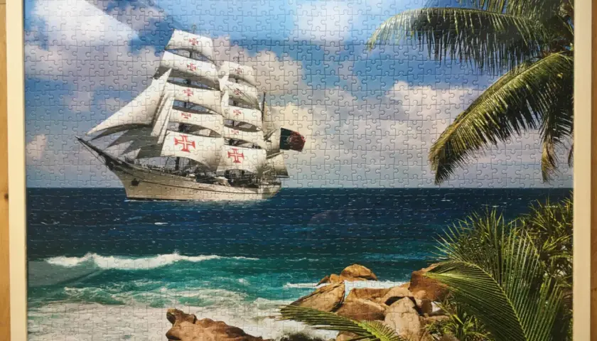 Ukończone puzzle na ścianie przedstawiają żaglowiec z czerwonymi krzyżami na białych żaglach, płynący po wzburzonym morzu.