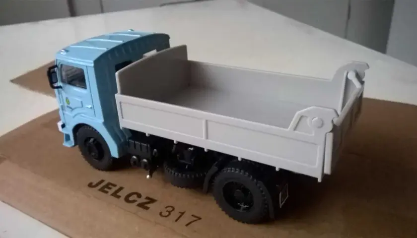 Model wywrotki Jelcz 317 w kolorze jasnoniebieskim, z szarą skrzynią ładunkową, stoi na kartonowym pudełku.