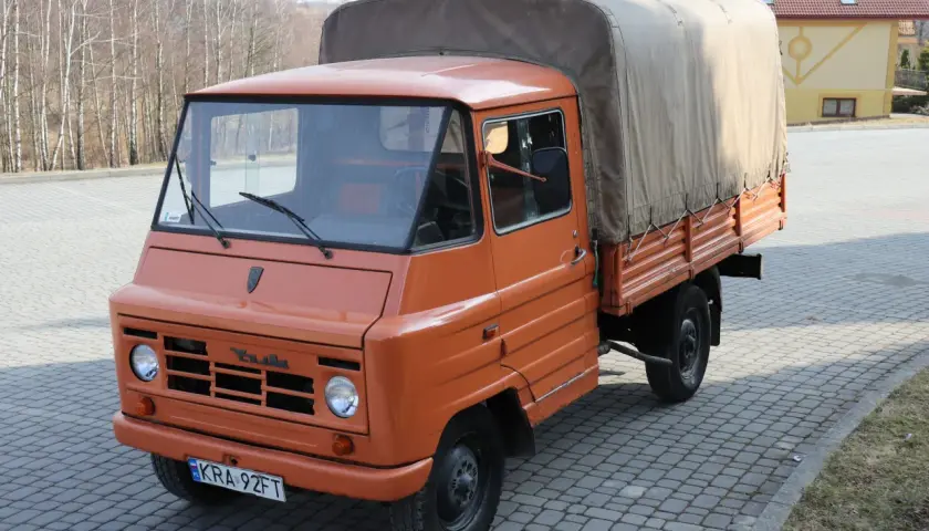 Pomarańczowy żuk z plandeką, gotowy do transportu towarów.