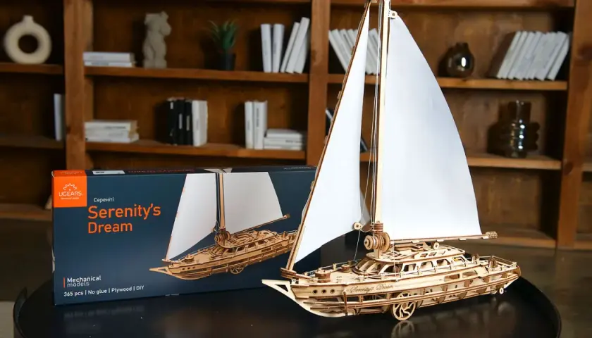 Drewniane modelarstwo: gotowy model żaglowca "Serenity's Dream" obok pudełka. Piękne detale i białe żagle.