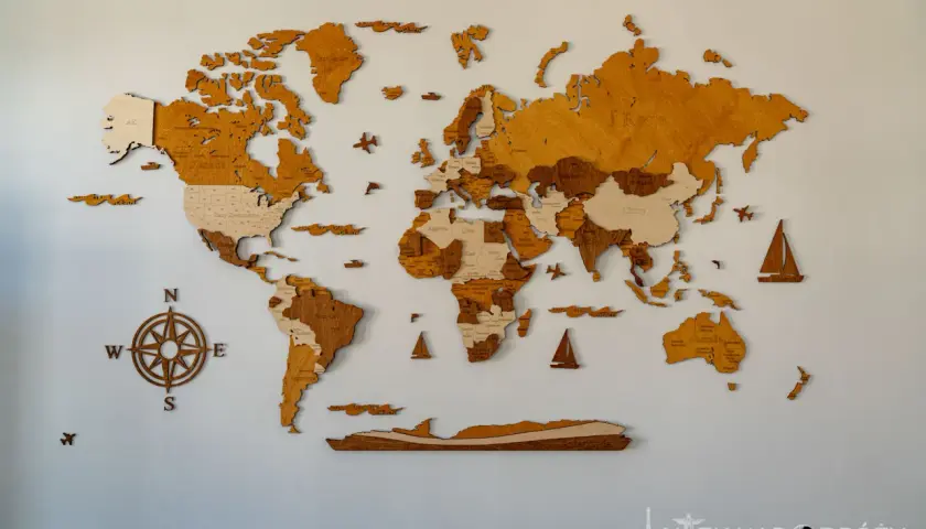 Drewniana mapa świata na ścianę, z zaznaczonymi krajami i oceanami. Kompas i żaglówki dodają jej podróżniczego charakteru.