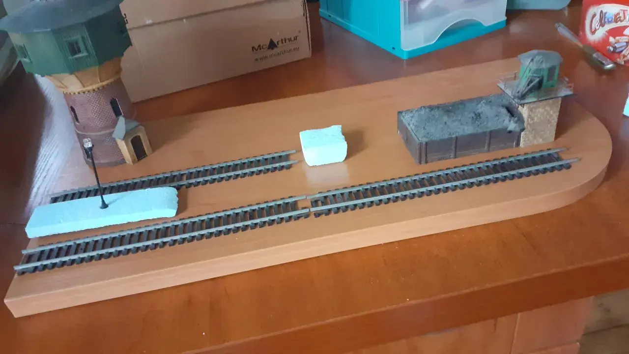 Diorama kolejowa z wieżą wodną, wagonem węglowym i budynkiem stacyjnym.