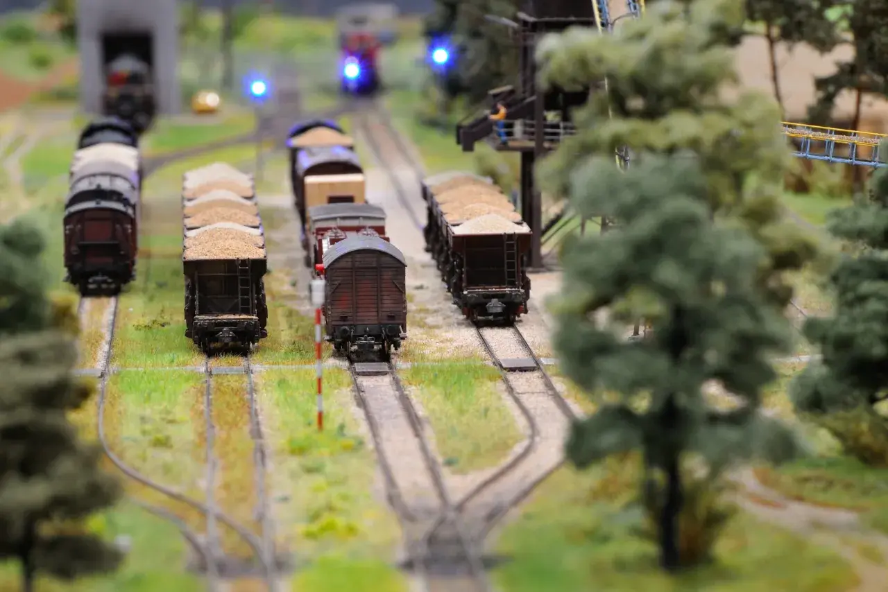 Miniaturowa kolej żelazna z wagonami towarowymi, zielenią i niebieskimi światłami sygnalizacyjnymi.