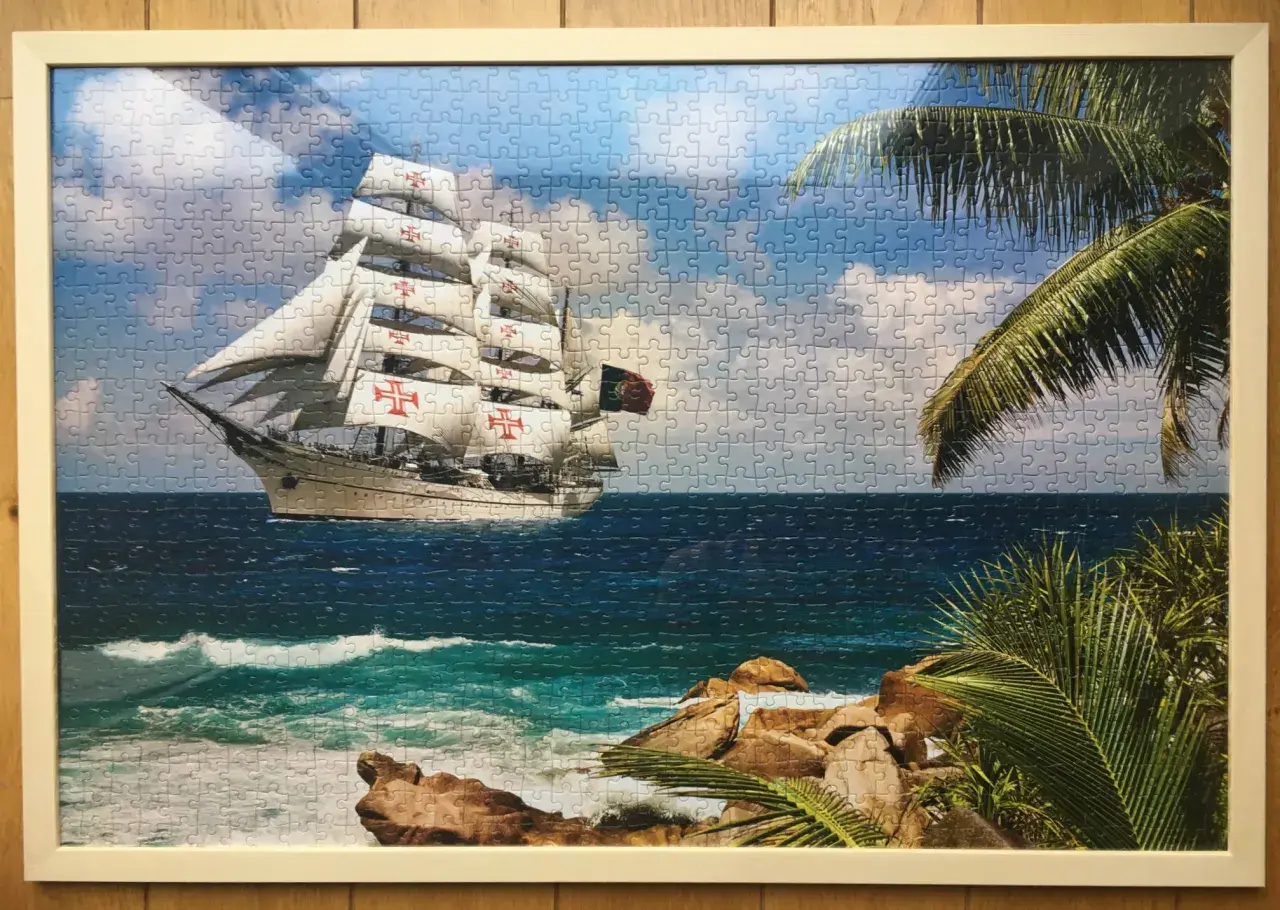Ukończone puzzle na ścianie przedstawiają żaglowiec z czerwonymi krzyżami na białych żaglach, płynący po wzburzonym morzu.