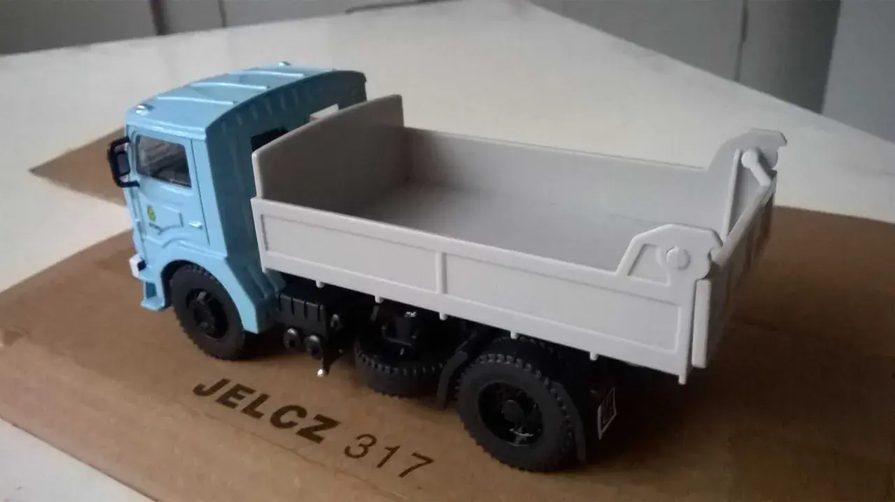 Model wywrotki Jelcz 317 w kolorze jasnoniebieskim, z szarą skrzynią ładunkową, stoi na kartonowym pudełku.