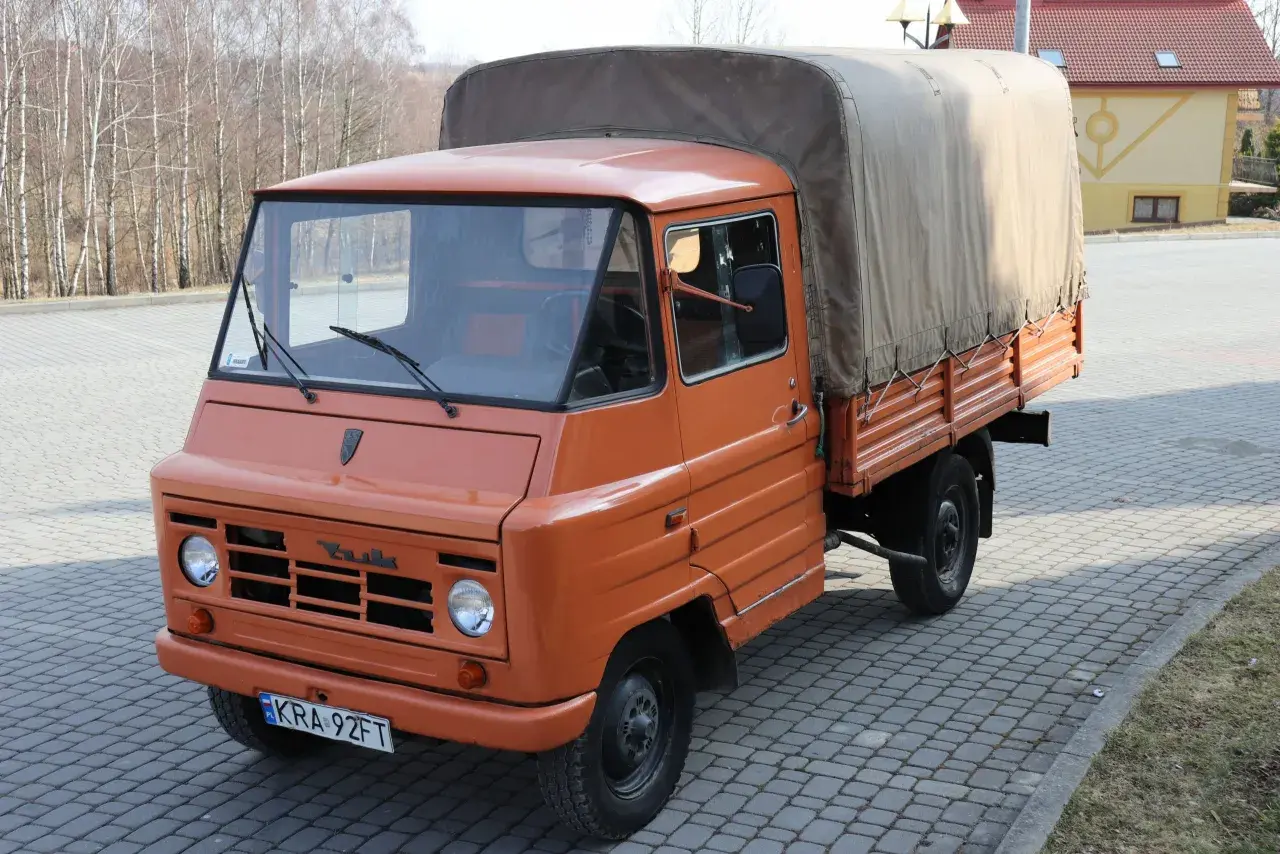 Pomarańczowy żuk z plandeką, gotowy do transportu towarów.