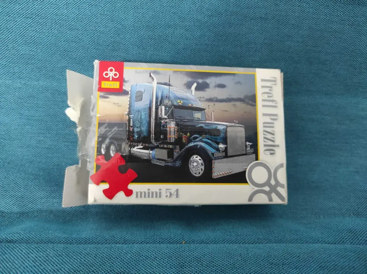 Pudełko z mini puzzlami przedstawiające niebieską ciężarówkę z chromowanymi detalami. Idealne dla miłośników motoryzacji i układania.