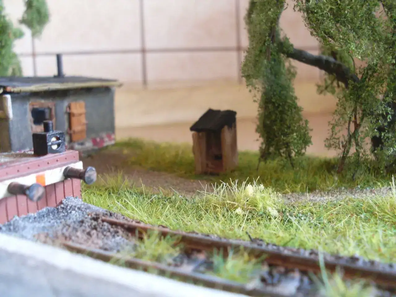Urocza diorama kolejowa z miniaturowym budynkiem, drzewami i torami.