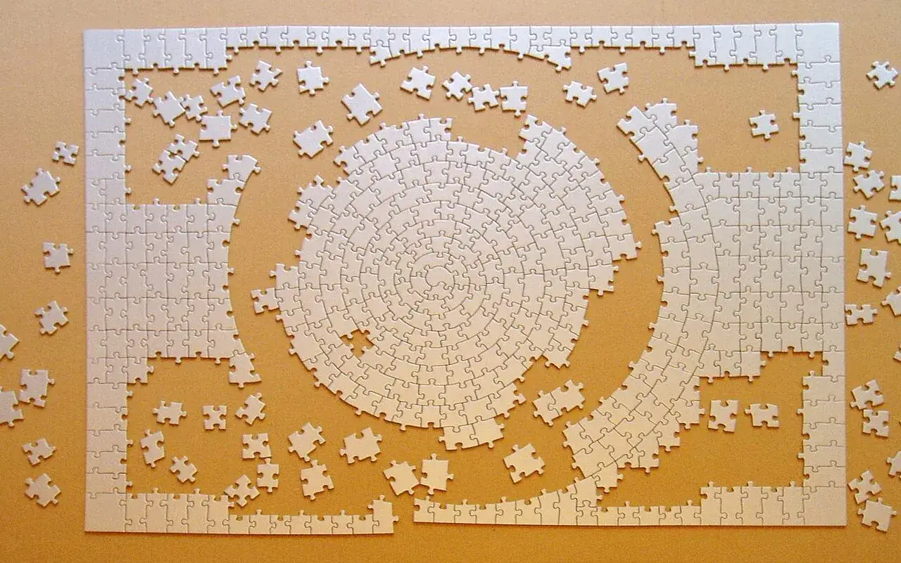 Białe, nieułożone elementy puzzli tworzą spiralę i prostokąt. R&oacute;żne rodzaje puzzli czekają na połączenie.