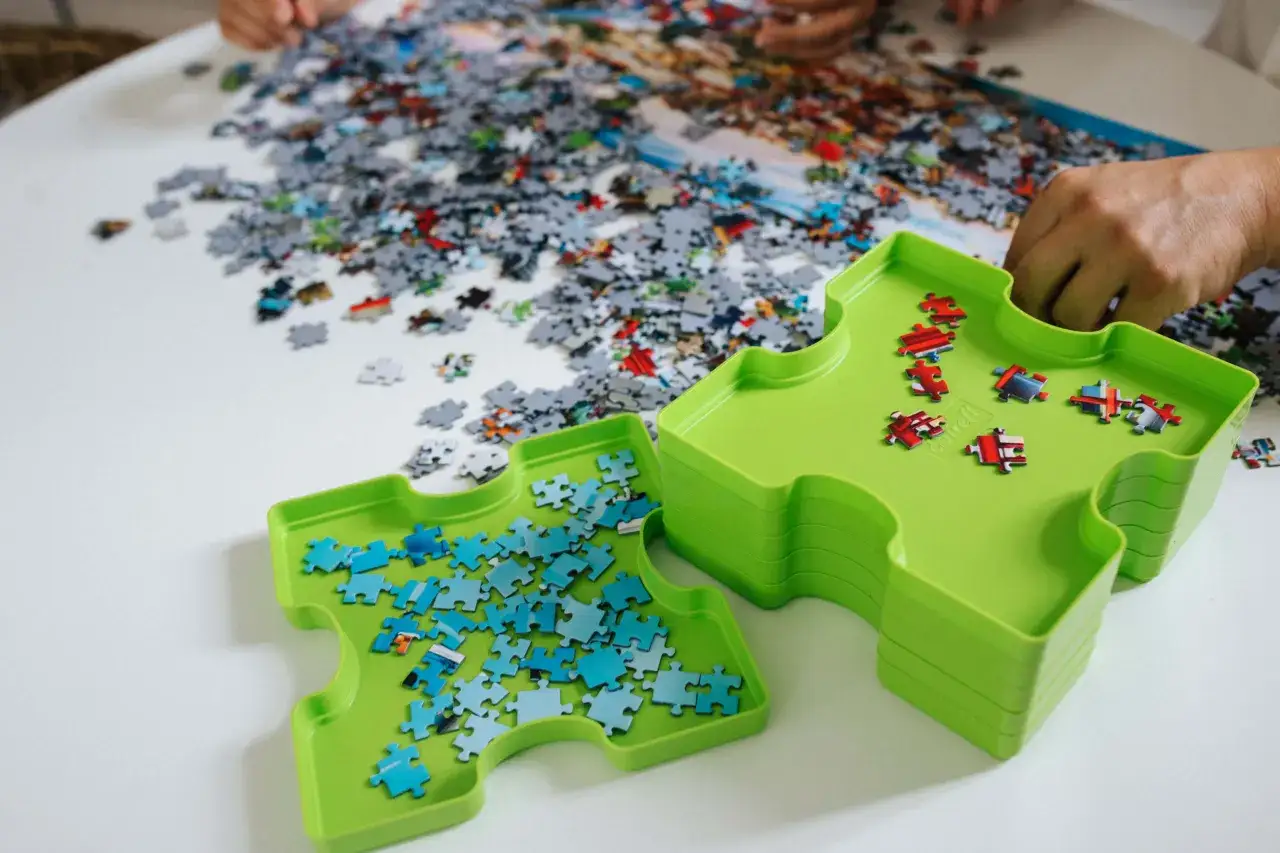 Ręce składają trudne puzzle na stole. Zielone tacki pomagają w sortowaniu element&oacute;w.