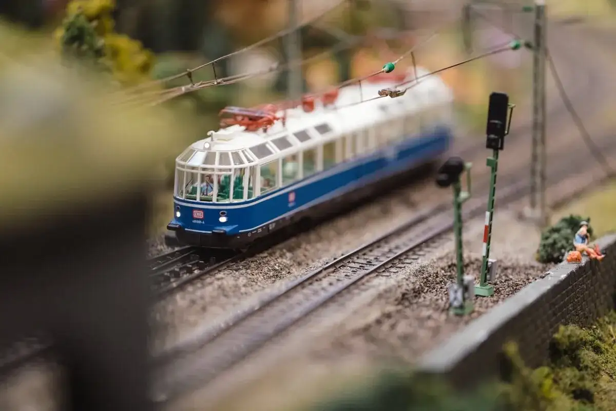Niebiesko-białe modele pociąg&oacute;w na miniaturowej trasie kolejowej, z semaforem i figurkami ludzi.