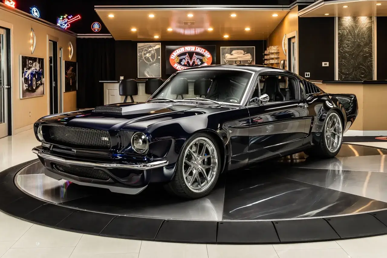 Lśniący, granatowy Ford Mustang '65 na obrotowej platformie, w garażu z neonami i zdjęciami klasycznych aut.