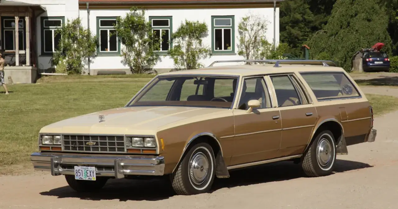 Klasyczny Chevrolet Impala w wersji kombi, dwukolorowy, brązowo-beżowy, zaparkowany przed domem.