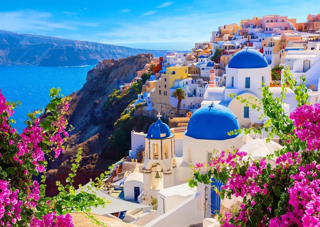 Widok na białe domy z niebieskimi kopułami, kwitnące bugenwille i morze. Jak układanka Santorini, która zachwyca.