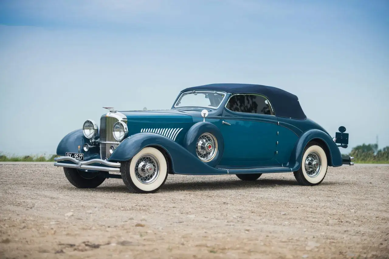 Elegancki, błękitny Duesenberg Model J z lat 30. XX wieku, z opuszczonym dachem, prezentuje się na tle błękitnego nieba.