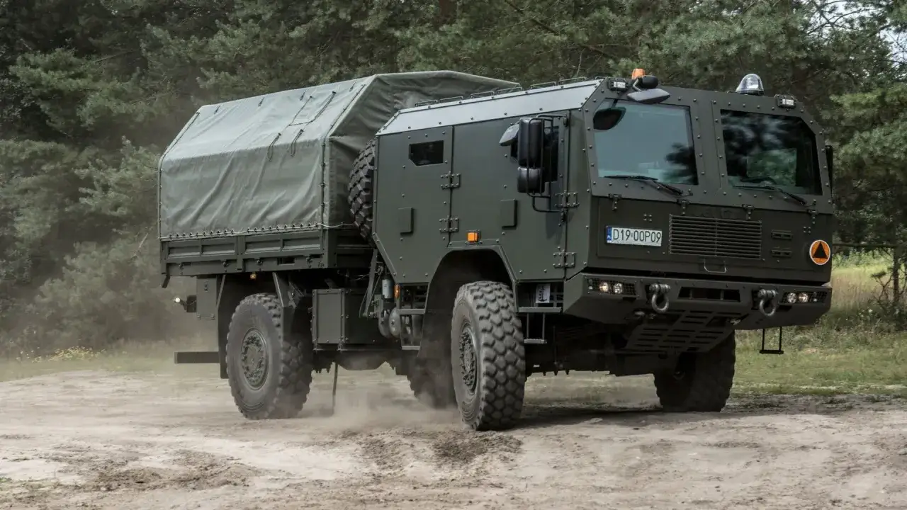 Potężny Jelcz 4x4 w wojskowej wersji, z plandeką na pace, przemierza piaszczystą drogę wśr&oacute;d drzew.