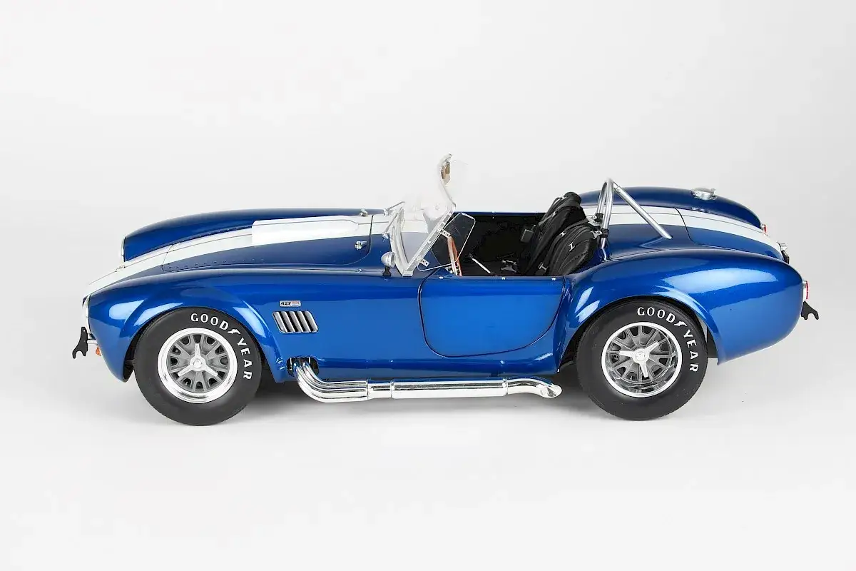 Błękitny Shelby Cobra 427 z białym pasem na masce, z chromowanymi rurami wydechowymi i oponami Goodyear.