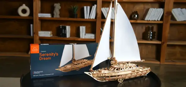 Drewniane modelarstwo: gotowy model żaglowca "Serenity's Dream" obok pudełka. Piękne detale i białe żagle.